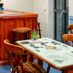 Pub-style bar with a wooden counter, bar stools and a table set with dominoes at Bridge House Care Home, Brighouse