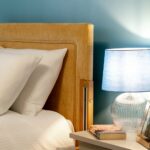 Bed with an ochre upholstered headboard beside a blue bedside lamp and books at Bridge House Care Home, Brighouse