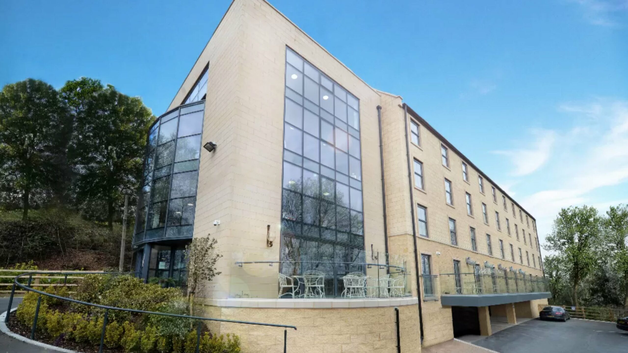 Modern stone-clad building with full-height glazing and a glass-railed terrace at Bridge House Care Home, Brighouse