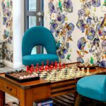 Games corner with a chess table, teal chairs and bird-patterned wallpaper at Bridge House Care Home, Brighouse