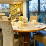 Dining room with round wooden tables laid for a meal beside floor-to-ceiling windows at Bridge House Care Home, Brighouse