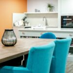 Kitchen and dining area with teal chairs, built-in ovens and an orange feature wall at Bridge House Care Home, Brighouse