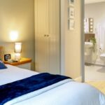 Bedroom with a navy throw, fitted wardrobe and an open door to the en-suite at Whitby Court Care Home, Whitby
