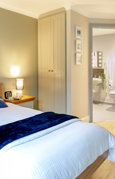 Bedroom with a navy throw, fitted wardrobe and an open door to the en-suite at Whitby Court Care Home, Whitby
