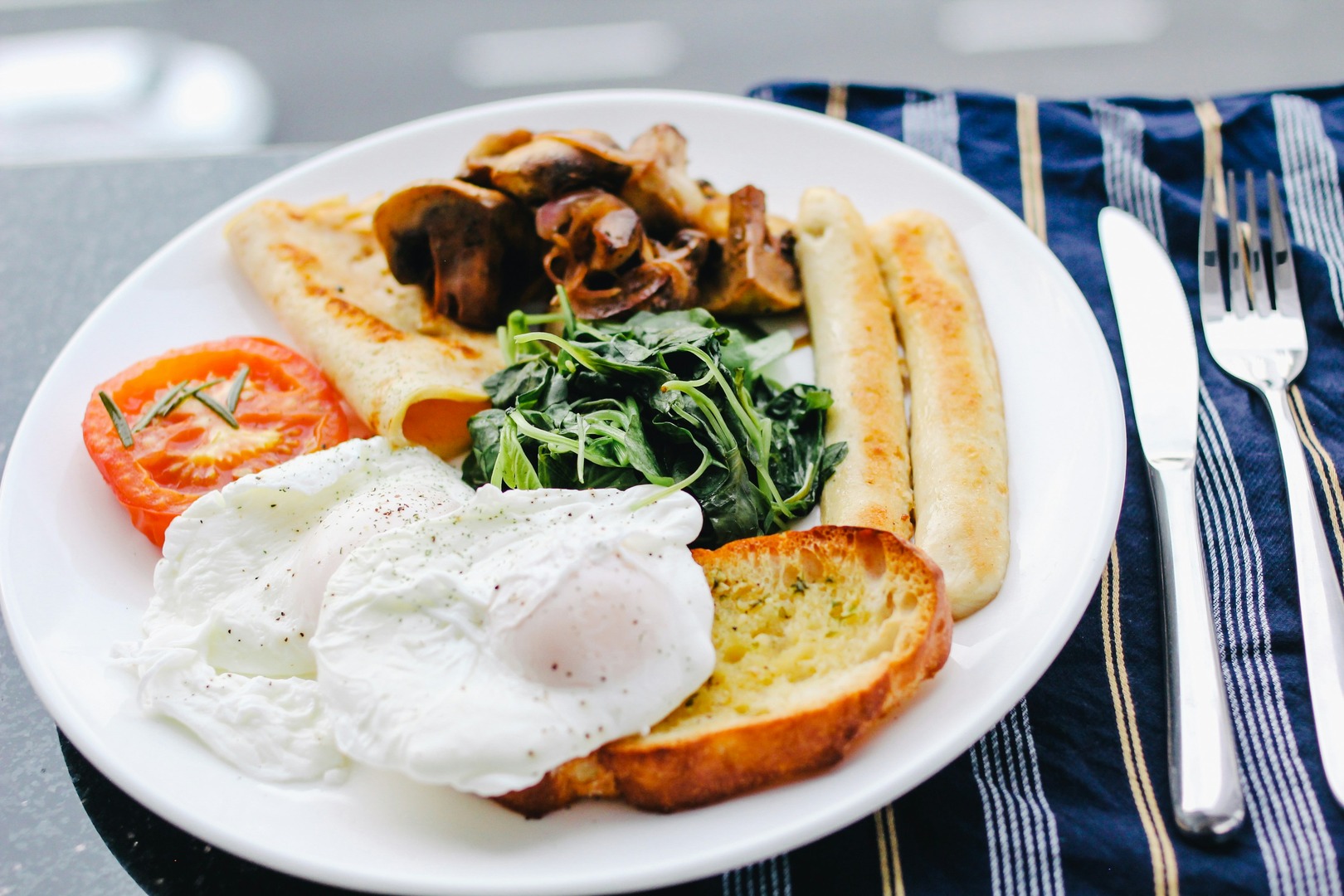 Breakfast plate of poached eggs, sausages, mushrooms, spinach, grilled tomato and toast