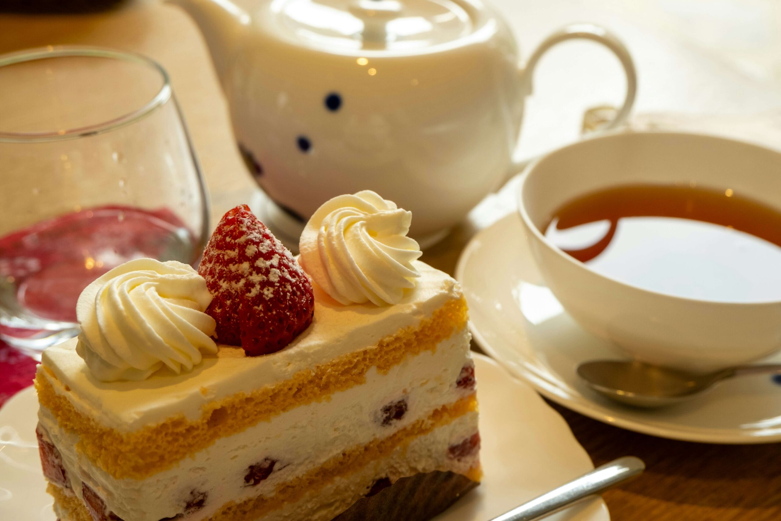 Slice of strawberry and cream layer cake beside a teapot and a cup of tea Slice of strawberry and cream layer cake beside a teapot and a cup of tea