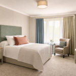 Artist's impression of a bedroom with upholstered headboard, armchair, desk and wardrobe at Elland Court Care Home, Leeds