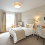 Single bedroom with dressing table, mirror and an armchair by the window at The Maltings Care Home, Bridlington