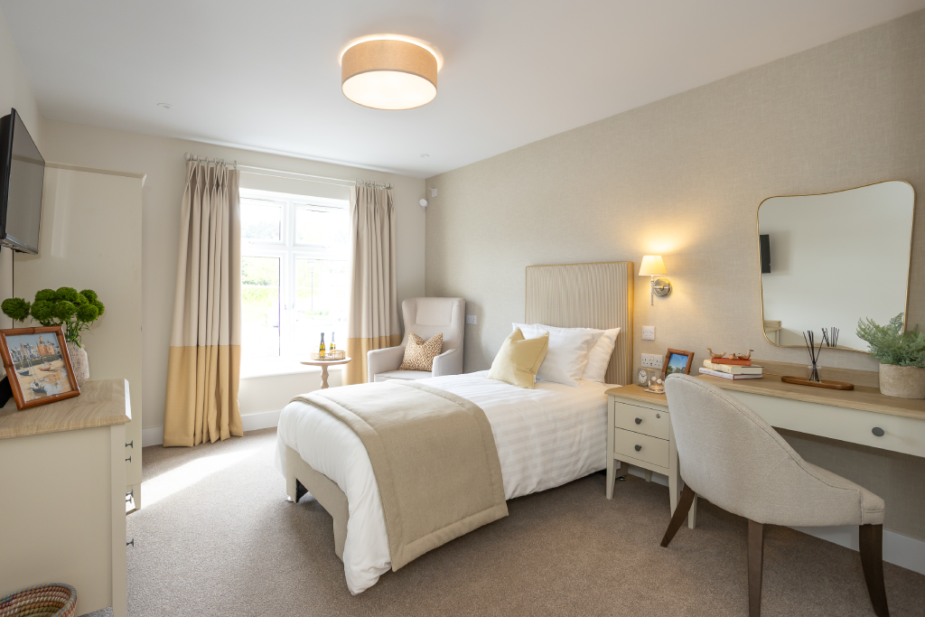 Single bedroom with dressing table, mirror and an armchair by the window at The Maltings Care Home, Bridlington