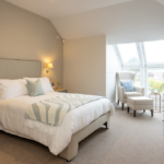 Double bedroom with sage bedside tables and an armchair by the dormer window at The Maltings Care Home, Bridlington
