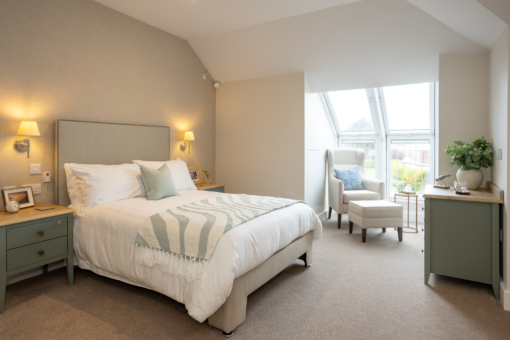 Double bedroom with sage bedside tables and an armchair by the dormer window at The Maltings Care Home, Bridlington