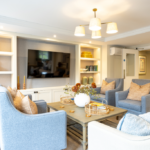 Lounge with built-in shelving, wall-mounted TV and blue armchairs at The Maltings Care Home, Bridlington