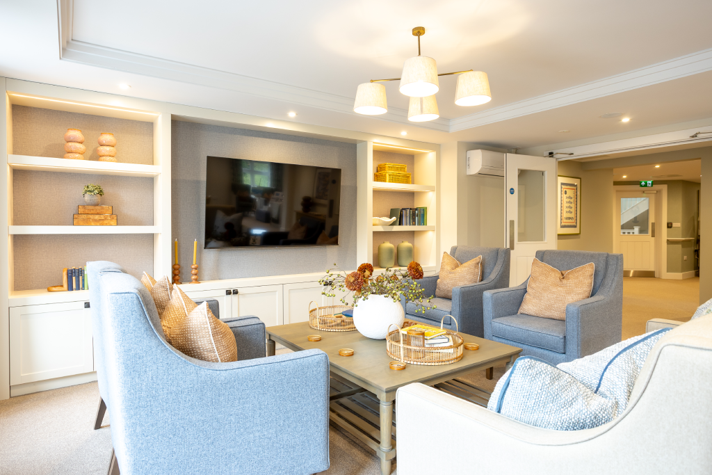 Lounge with built-in shelving, wall-mounted TV and blue armchairs at The Maltings Care Home, Bridlington