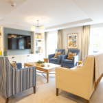 Lounge with striped armchairs, cream sofa and large windows at The Maltings Care Home, Bridlington