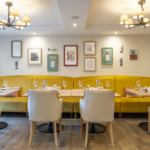 Dining room with yellow banquette seating, laid tables and chandeliers at The Maltings Care Home, Bridlington