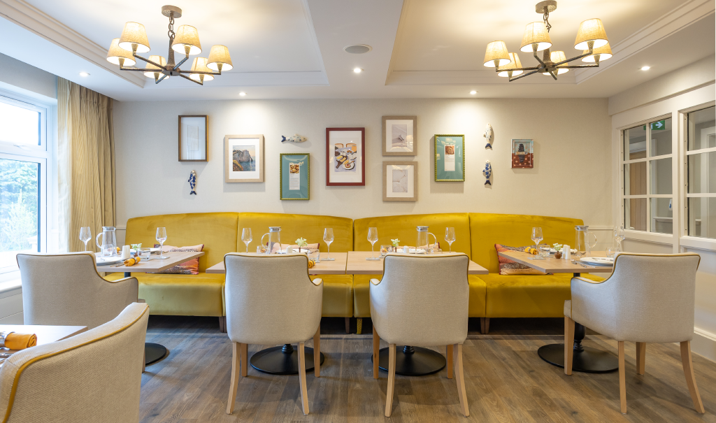 Dining room with yellow banquette seating, laid tables and chandeliers at The Maltings Care Home, Bridlington