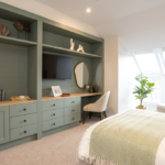 Bedroom with sage green fitted shelving, wall-mounted TV and desk at The Maltings Care Home, Bridlington