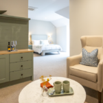 Suite sitting area with sage sideboard and armchairs, with the bedroom beyond at The Maltings Care Home, Bridlington