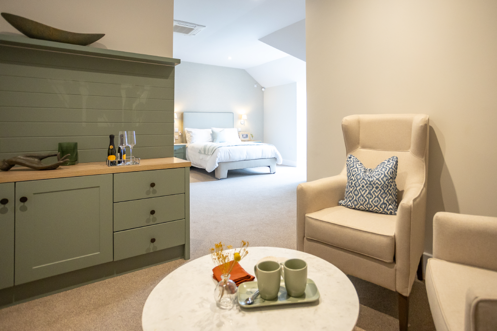 Suite sitting area with sage sideboard and armchairs, with the bedroom beyond at The Maltings Care Home, Bridlington