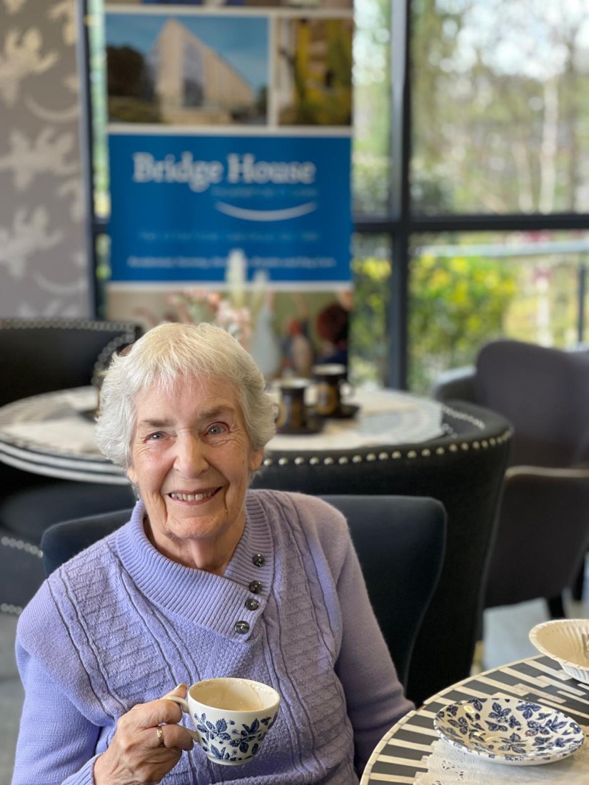 Smiling woman in a lilac jumper enjoying a cup of tea at Bridge House Care Home, Brighouse Smiling woman in a lilac jumper enjoying a cup of tea at Bridge House Care Home, Brighouse