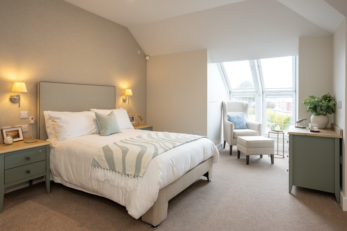 Bedroom with double bed, wall lights and an armchair by a large window at The Maltings Care Home, Bridlington