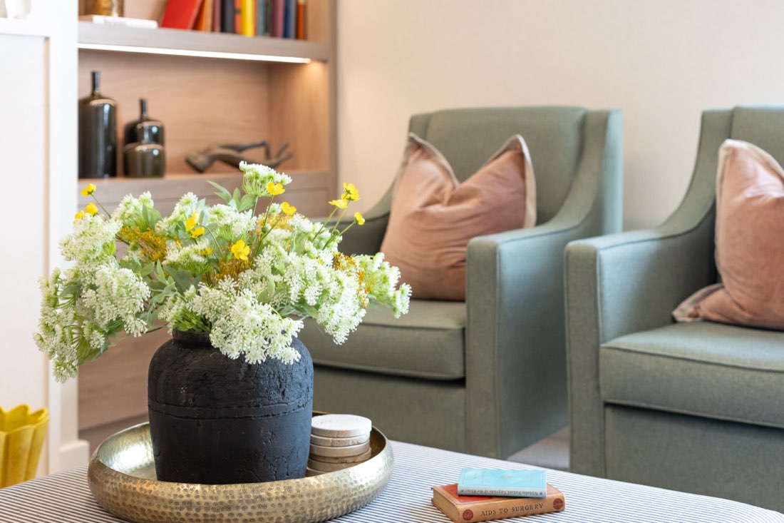 Sage-green armchairs with pink cushions beside a vase of wild flowers in a lounge at The Maltings Care Home, Bridlington