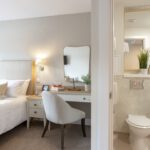 Bedroom with single bed and dressing table beside an en-suite with toilet and basin at The Maltings Care Home, Bridlington