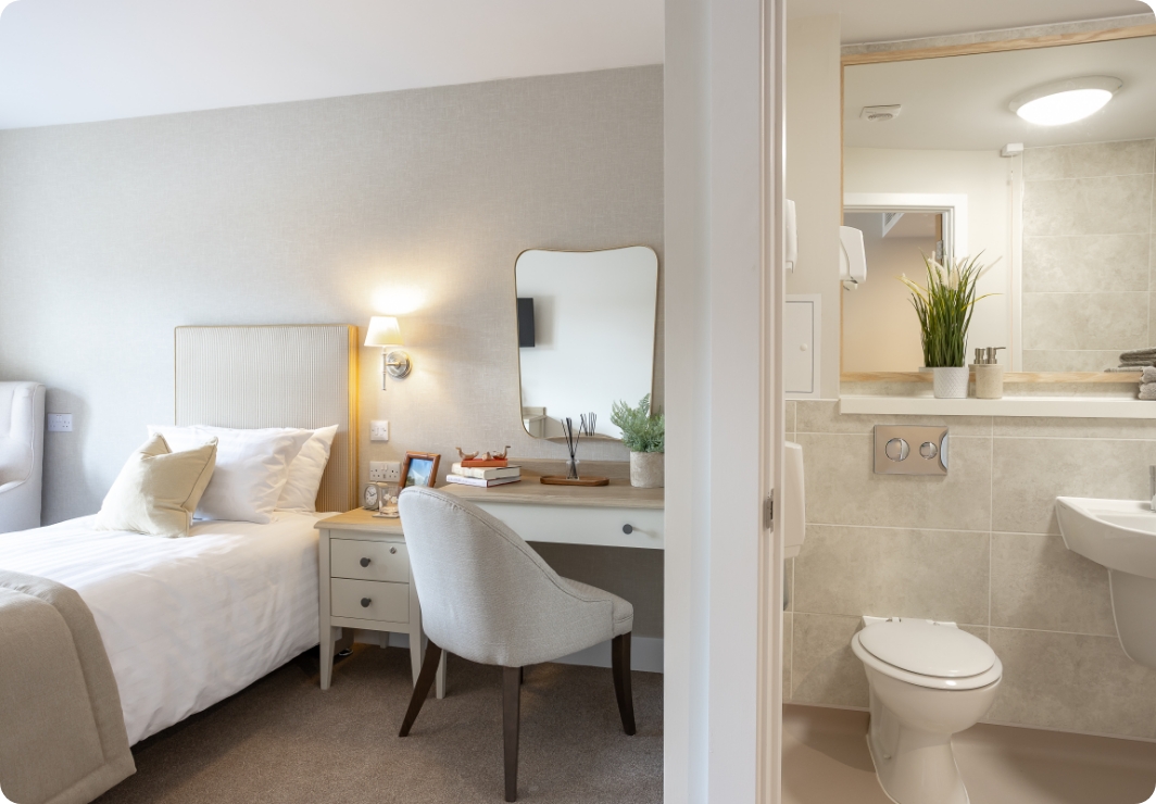Bedroom with single bed and dressing table beside an en-suite with toilet and basin at The Maltings Care Home, Bridlington Bedroom with single bed and dressing table beside an en-suite with toilet and basin at The Maltings Care Home, Bridlington
