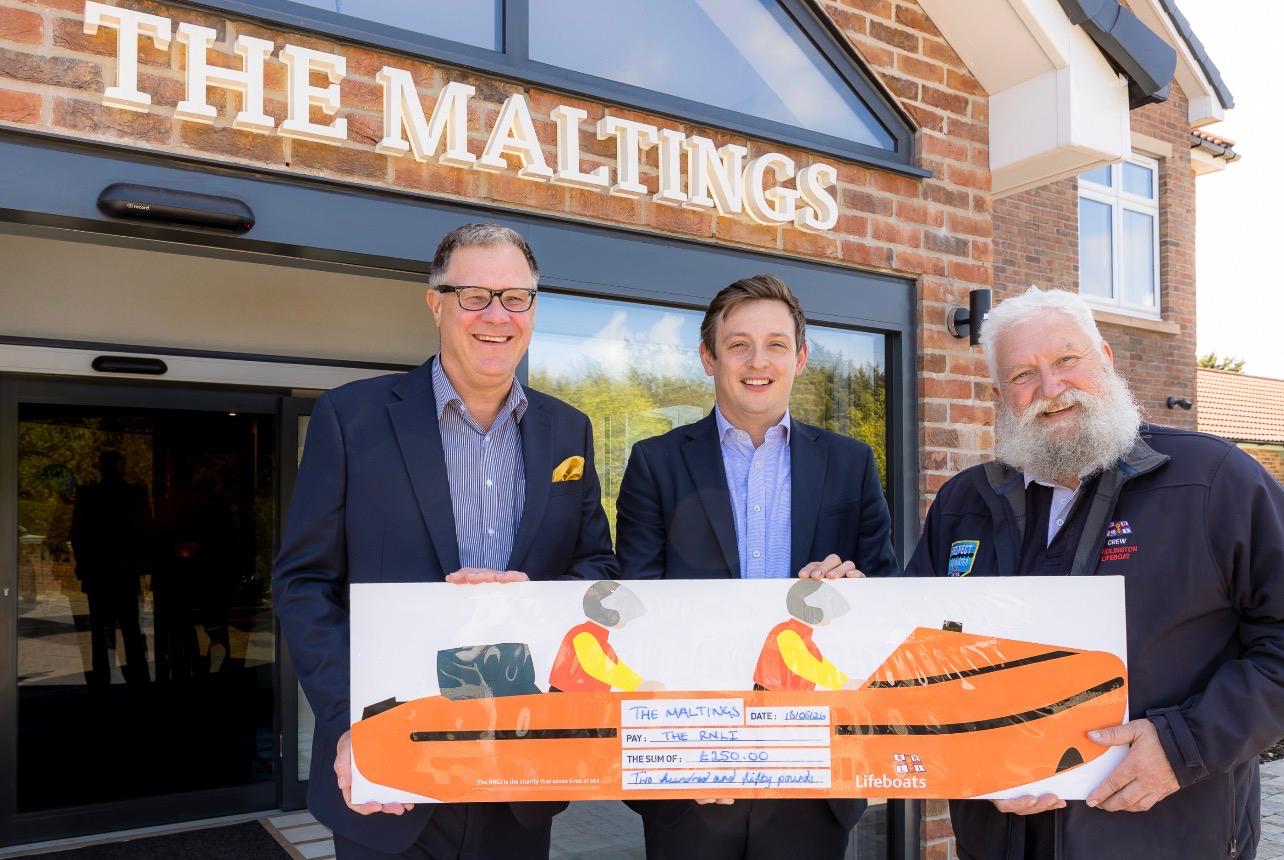 Two men in suits and a Bridlington lifeboat crew member holding a £250 RNLI cheque outside The Maltings Care Home, Bridlington