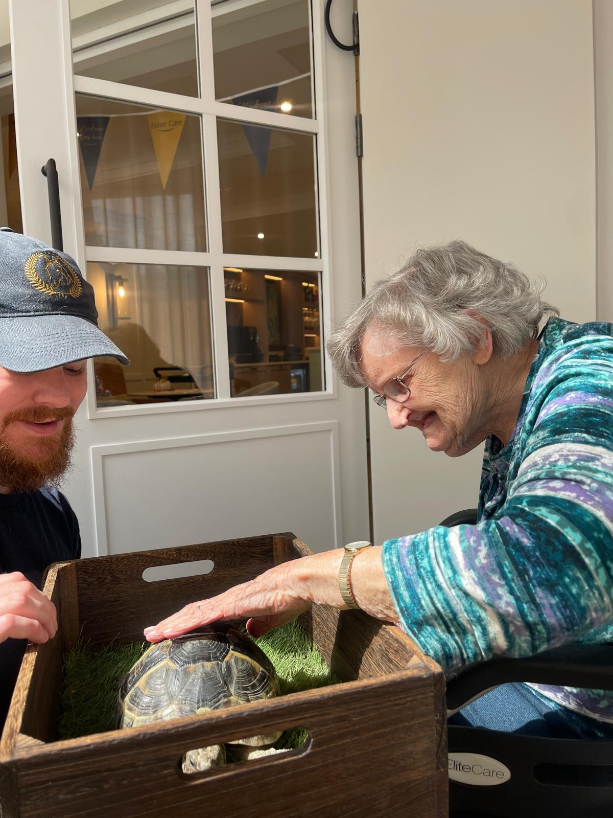 A Fisher Care resident smiling as she strokes a tortoise during a Fisher Care Moment