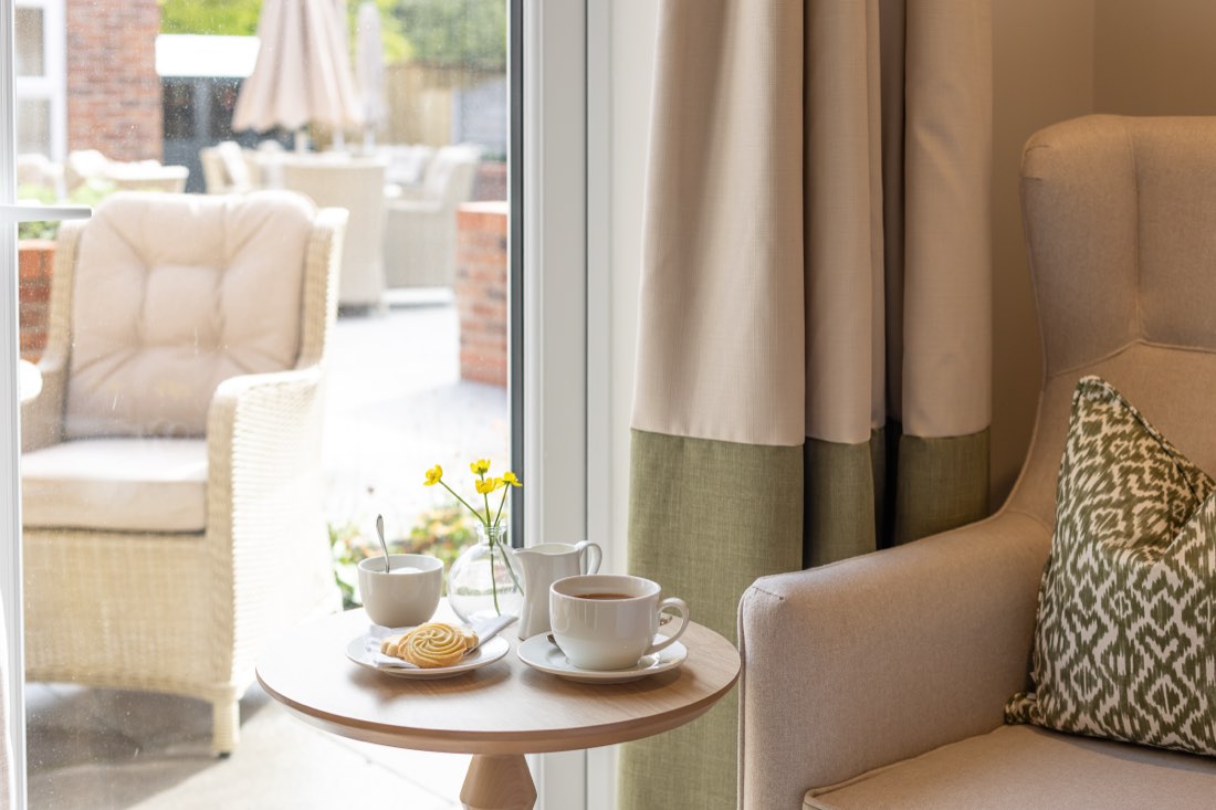 Tea and a biscuit on a side table by the patio doors, with garden seating outside, at The Maltings Care Home, Bridlington Tea and a biscuit on a side table by the patio doors, with garden seating outside, at The Maltings Care Home, Bridlington