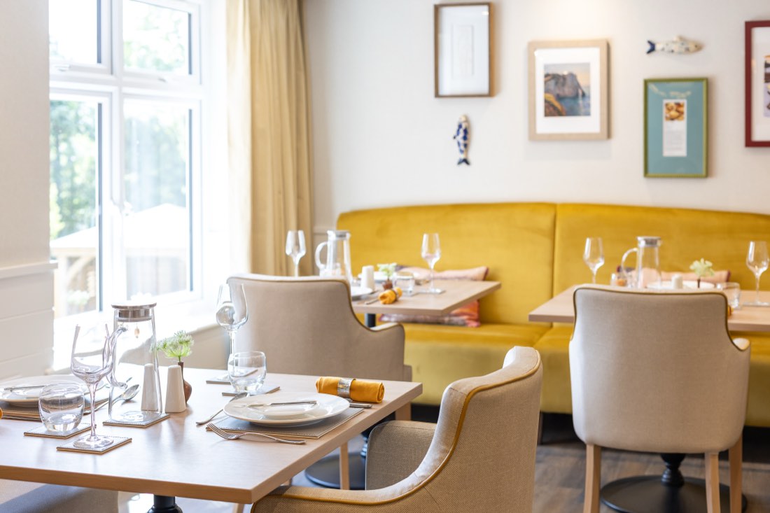 Dining room with yellow banquette seating and tables laid for a meal at The Maltings Care Home, Bridlington Dining room with yellow banquette seating and tables laid for a meal at The Maltings Care Home, Bridlington