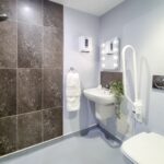 Accessible en-suite wet room with shower, basin and fold-down grab rail at Whitby Court Care Home, Whitby