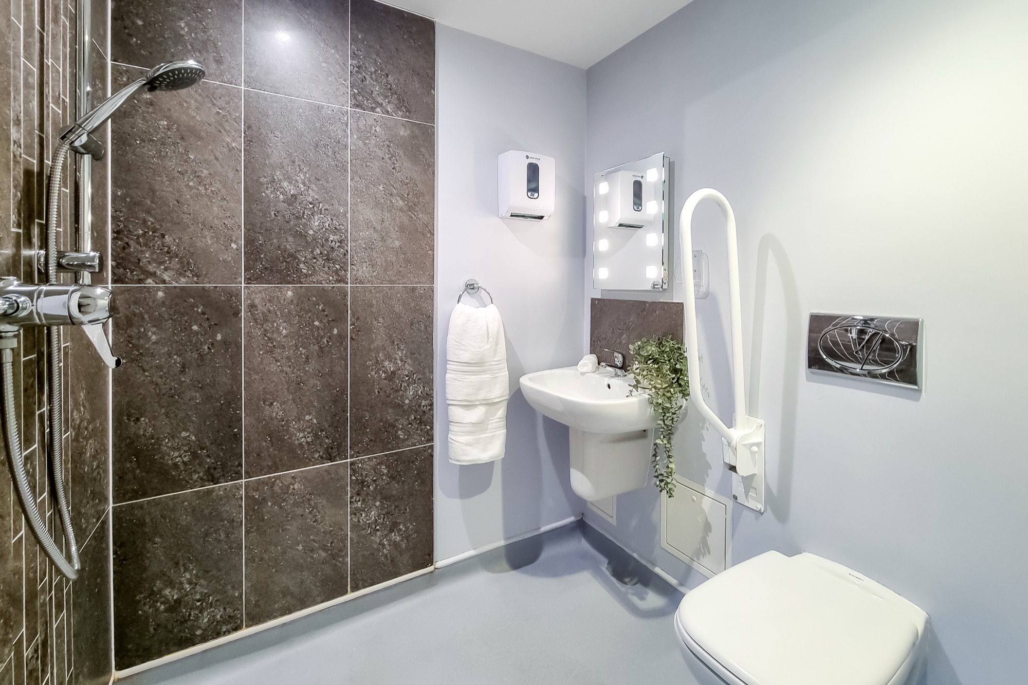 Accessible en-suite wet room with shower, basin and fold-down grab rail at Whitby Court Care Home, Whitby