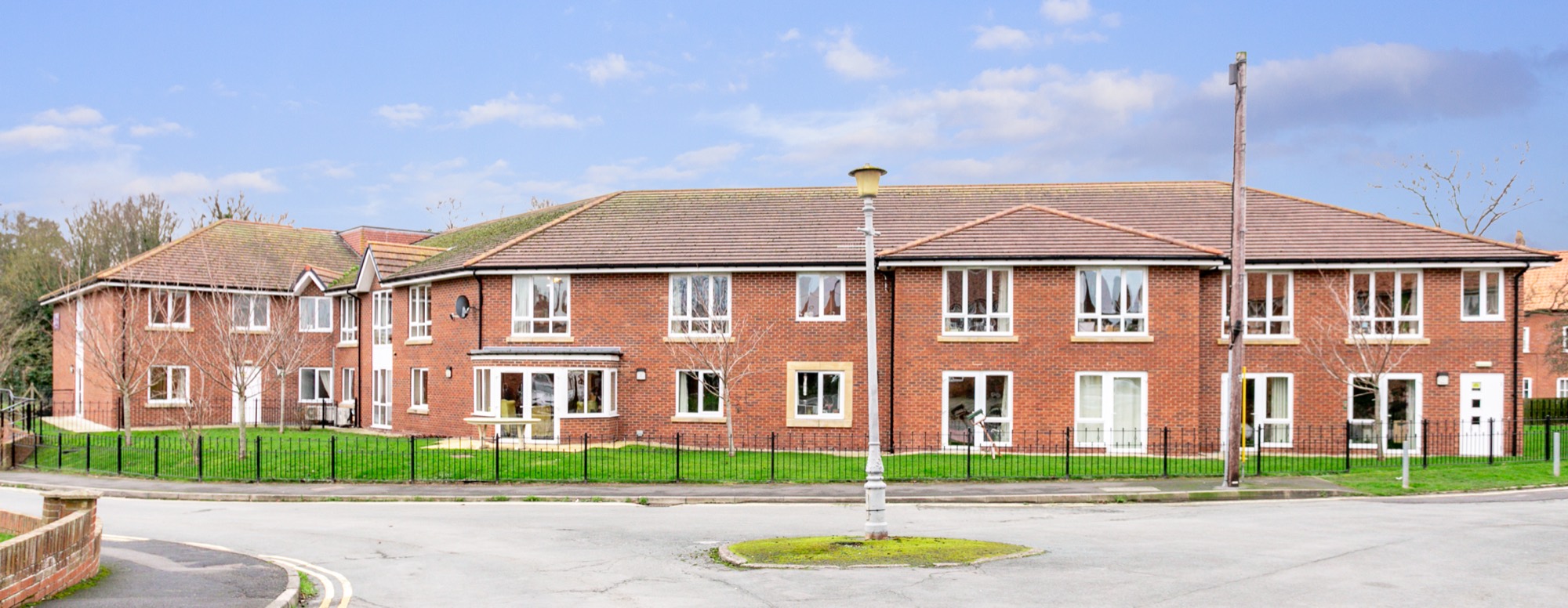 Wide view of the two-storey red-brick front and railed front lawn at Whitby Court Care Home, Whitby