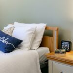 Bedside table with a book, reading glasses, clock and lit lamp at Whitby Court Care Home, Whitby
