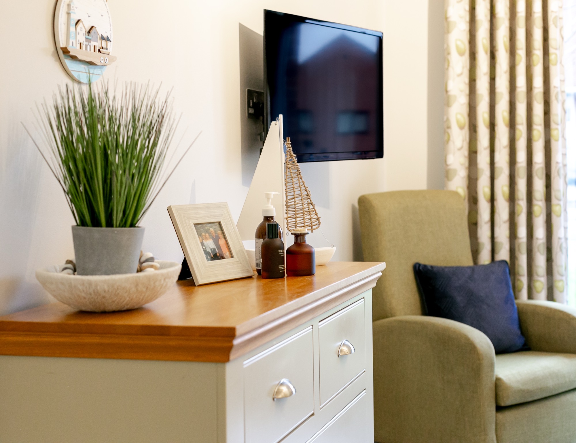 Bedroom with chest of drawers, armchair and wall-mounted TV at Whitby Court Care Home, Whitby