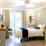 Bright bedroom with patio doors, armchair and single bed at Whitby Court Care Home, Whitby