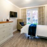 Spacious bedroom with patio doors, chest of drawers and armchair at Whitby Court Care Home, Whitby