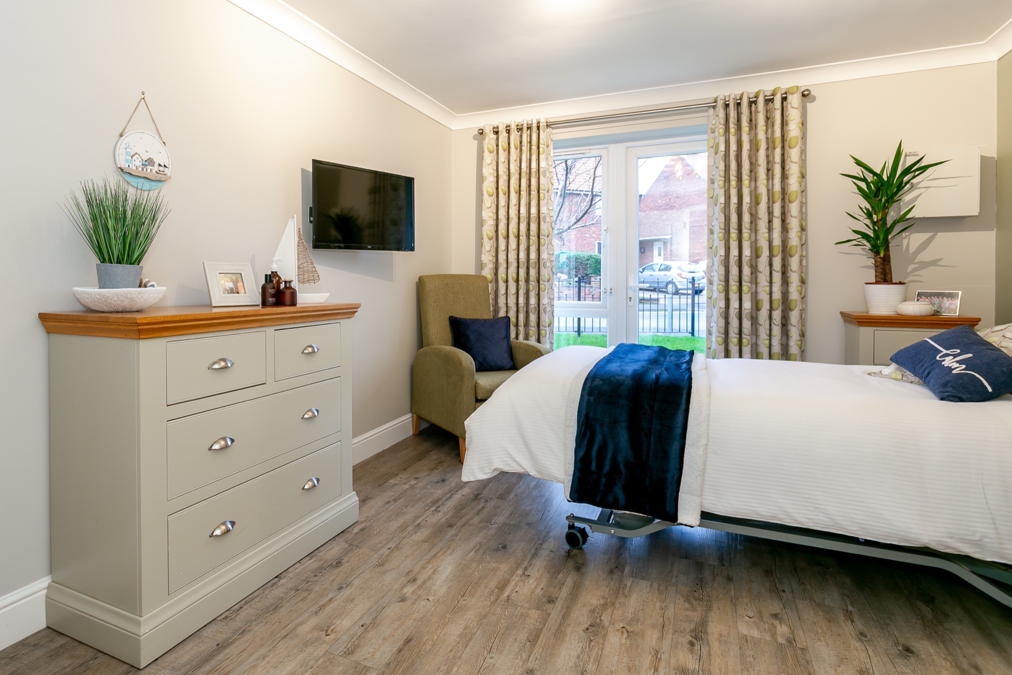 Spacious bedroom with patio doors, chest of drawers and armchair at Whitby Court Care Home, Whitby