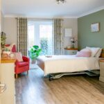 View through the open door into a bedroom with a red armchair and patio doors at Whitby Court Care Home, Whitby