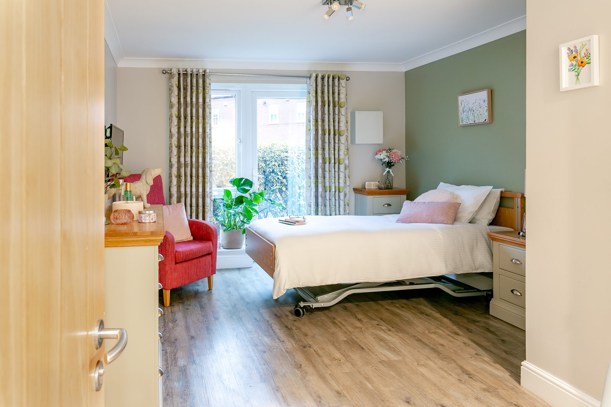 View through the open door into a bedroom with a red armchair and patio doors at Whitby Court Care Home, Whitby