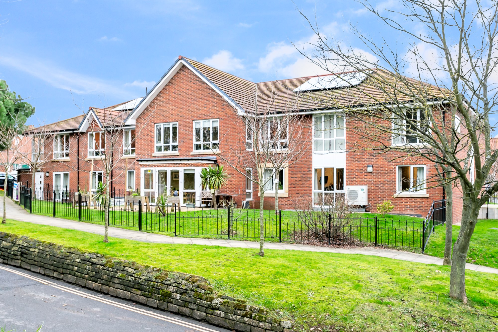 Two-storey red-brick exterior with railed front lawns and patio seating at Whitby Court Care Home, Whitby